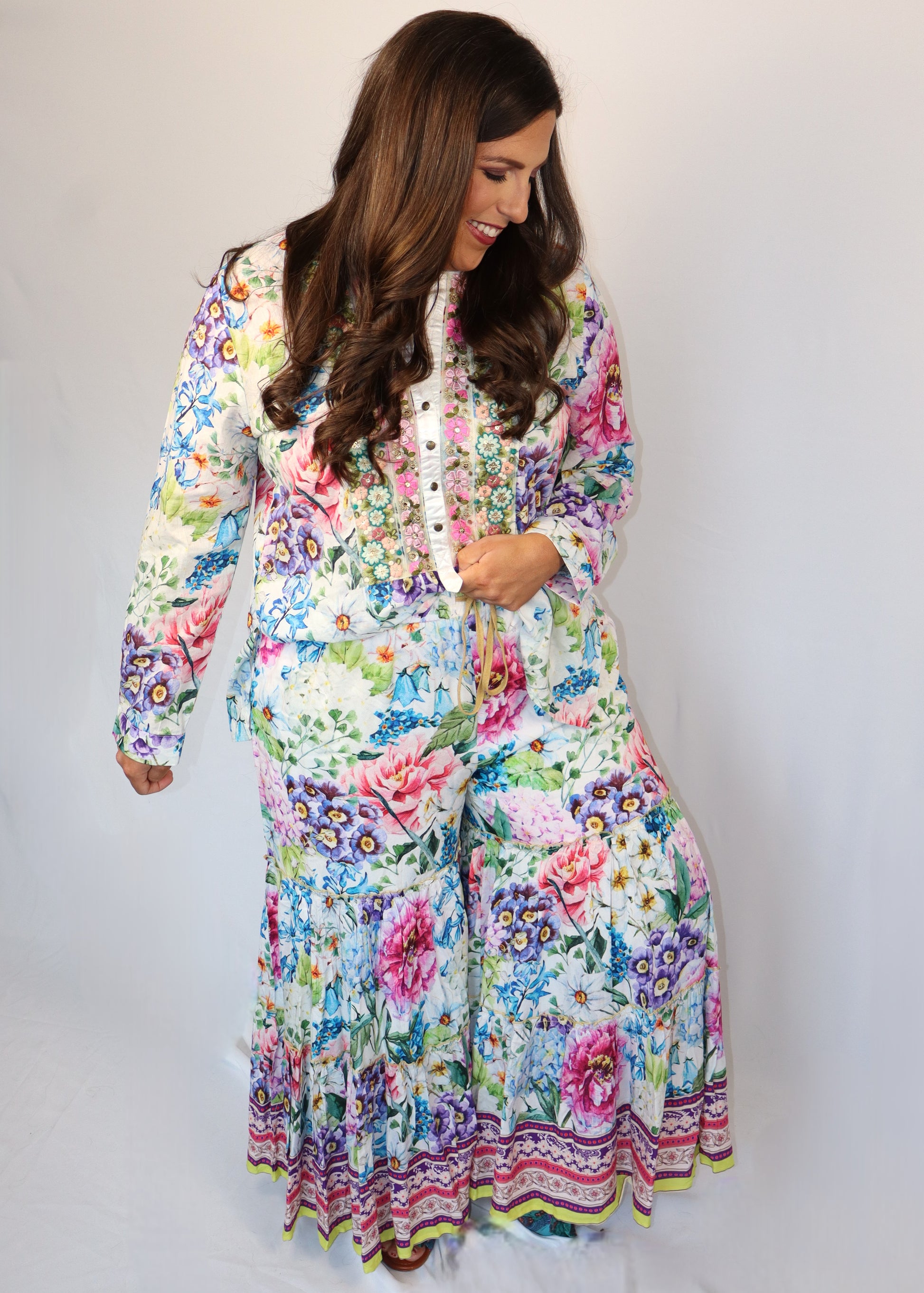 Woman wearing a matching floral blouse and flowy pants against a white background