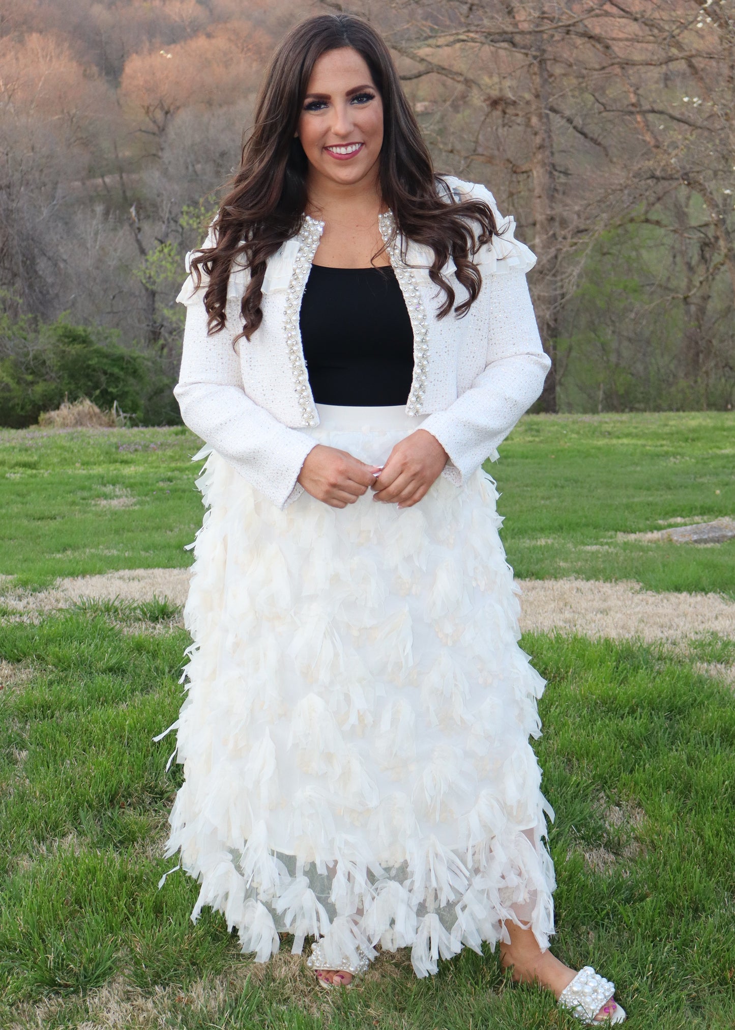 Woman wearing an ivory feathered skirt and ivory tweed jacket with a black top outdoors.