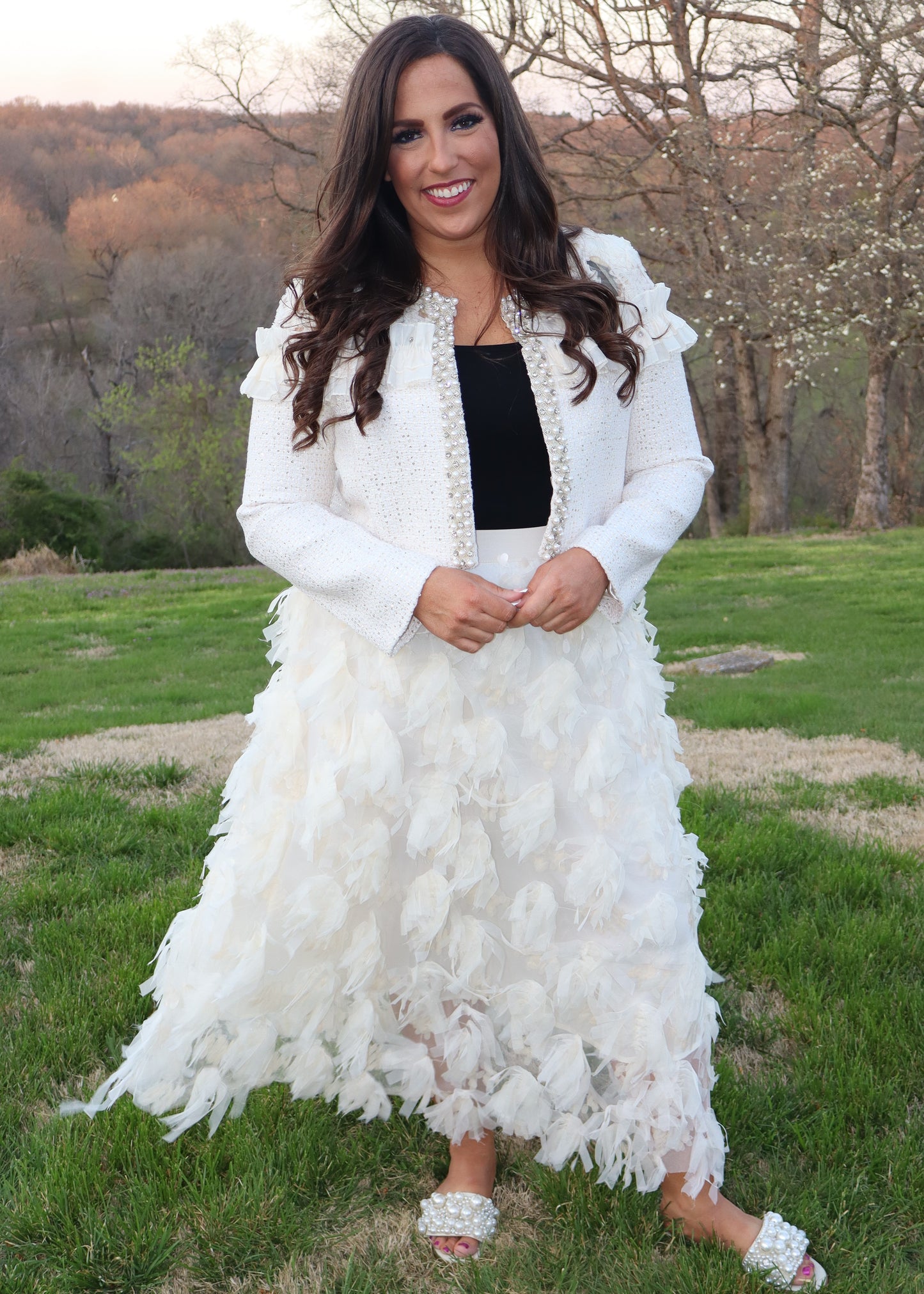 Woman wearing an ivory feathered skirt and ivory tweed jacket with a black top outdoors.