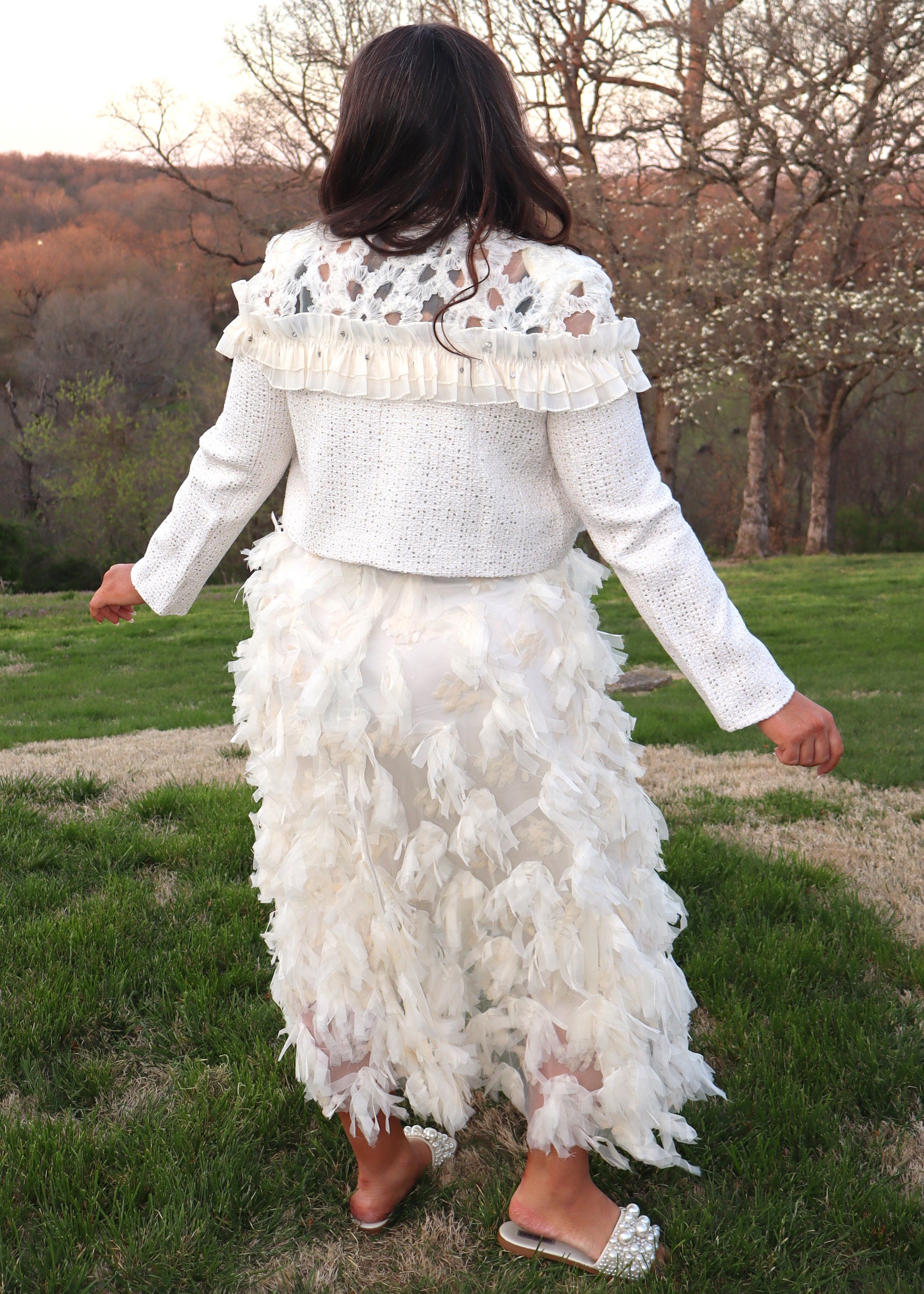 Woman wearing an ivory feathered skirt and ivory tweed jacket with a black top outdoors.
