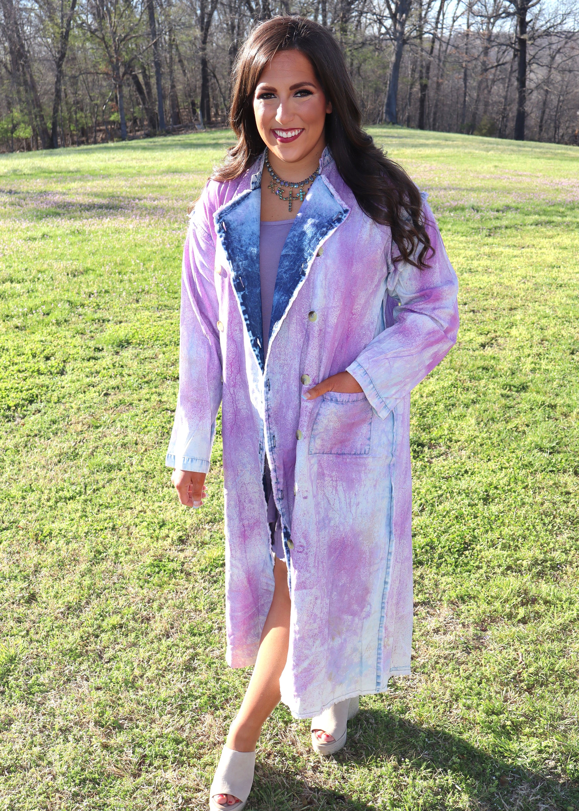 Woman wearing a purple and denim tie-dye painter's jacket outdoors on a grassy field