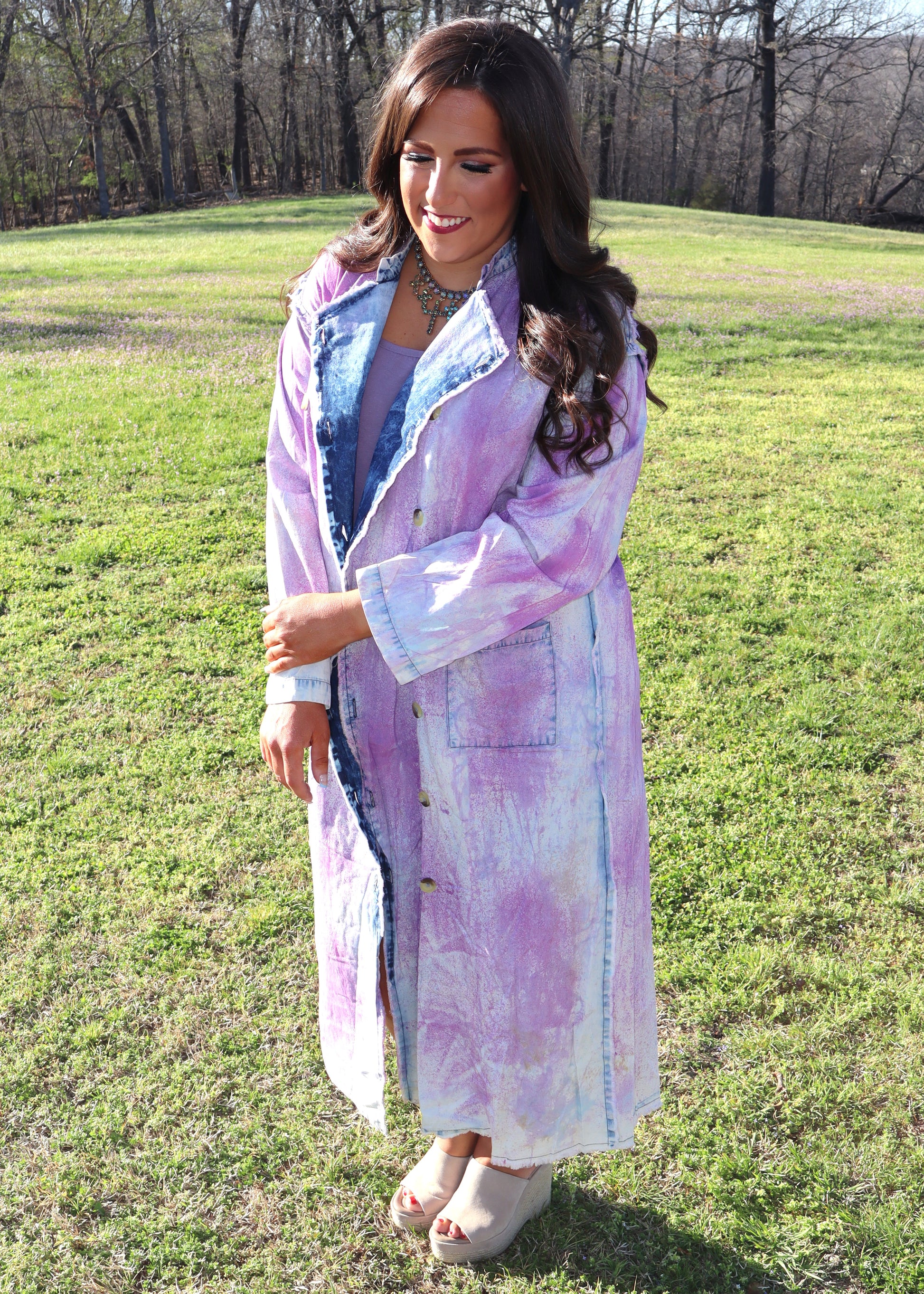Woman wearing a purple and denim tie-dye painter's jacket outdoors on a grassy field
