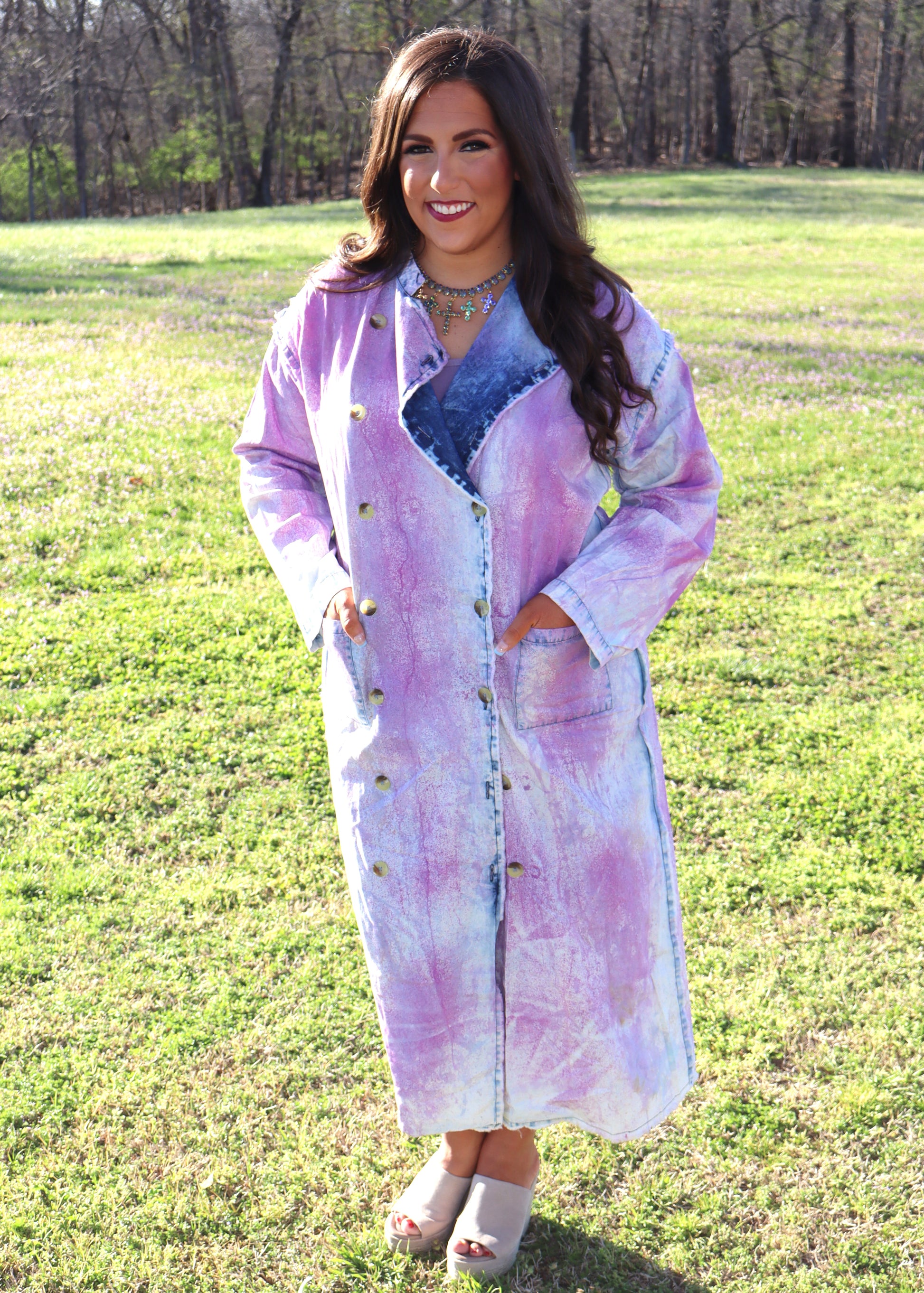 Woman wearing a purple and denim tie-dye painter's jacket outdoors on a grassy field