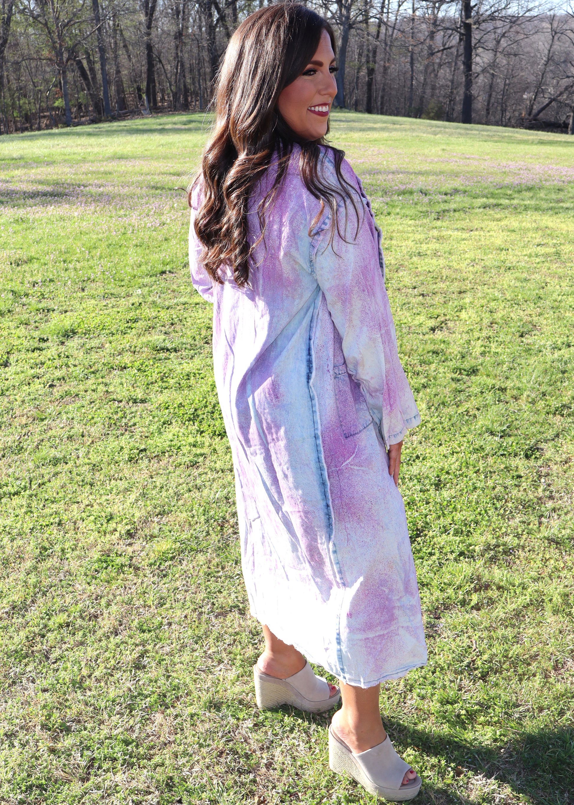Woman wearing a purple and denim tie-dye painter's jacket outdoors on a grassy field