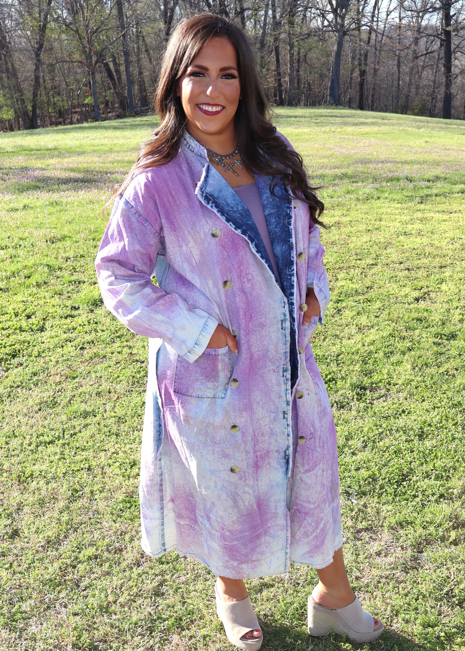 Woman wearing a purple and denim tie-dye painter's jacket outdoors on a grassy field