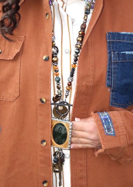 Woman wearing a chestnut brown button-up shirt with a beaded, long necklace and creepy vintage photo pendant and rustic key pendant.