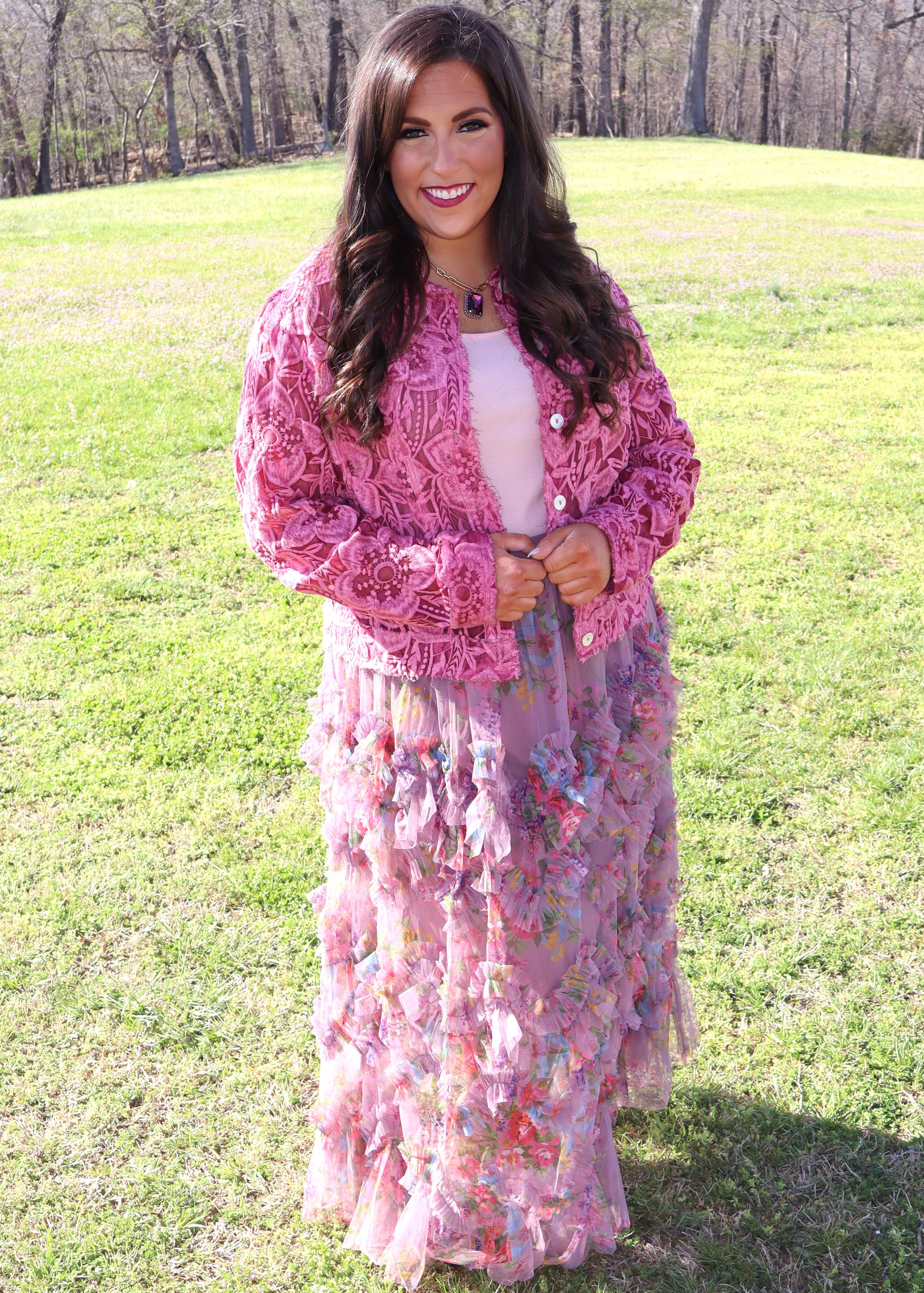Woman wearing a pink lace cardigan over a floral tulle skirt in an outdoor setting.