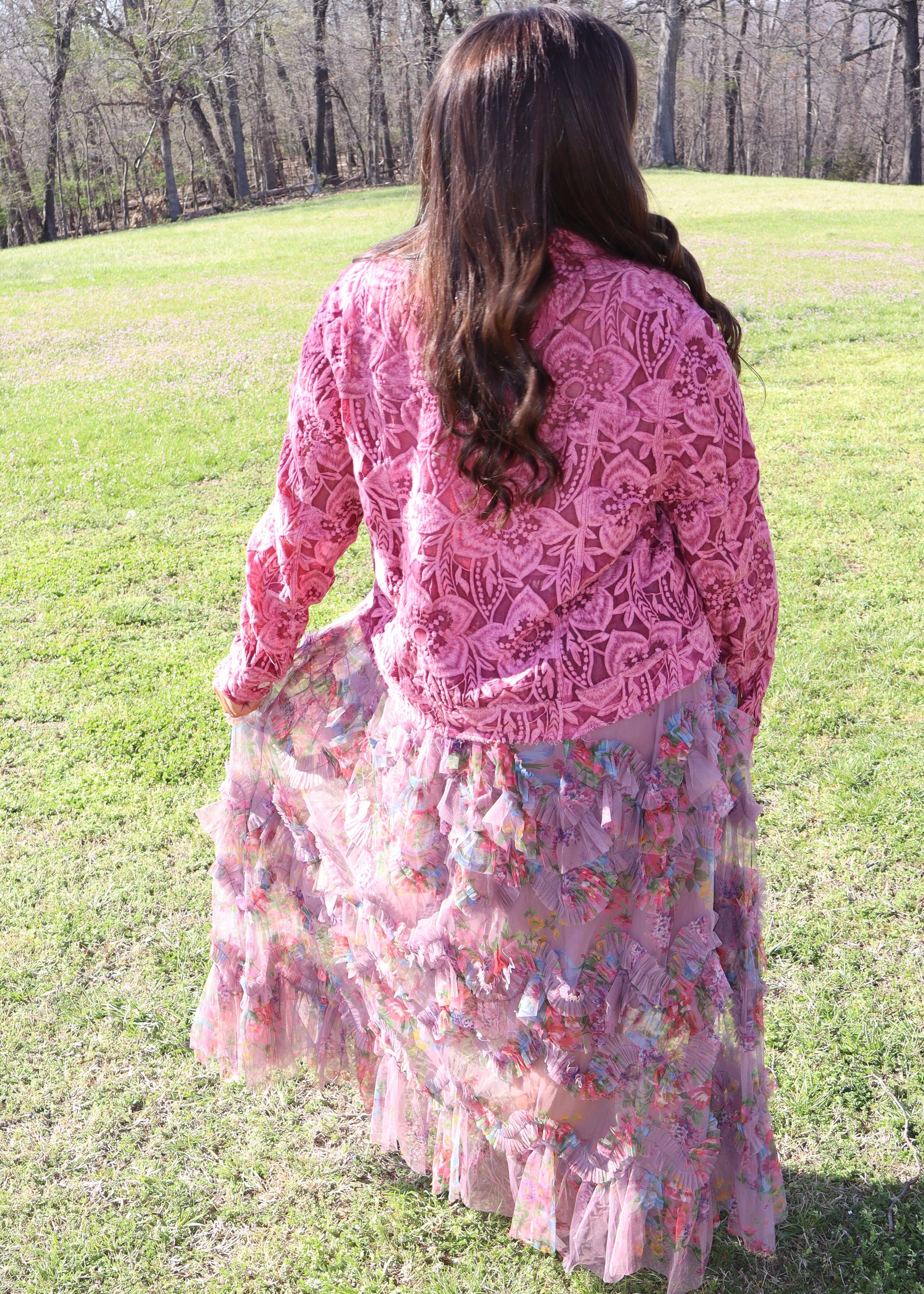 Woman wearing a pink lace cardigan over a floral tulle skirt in an outdoor setting.