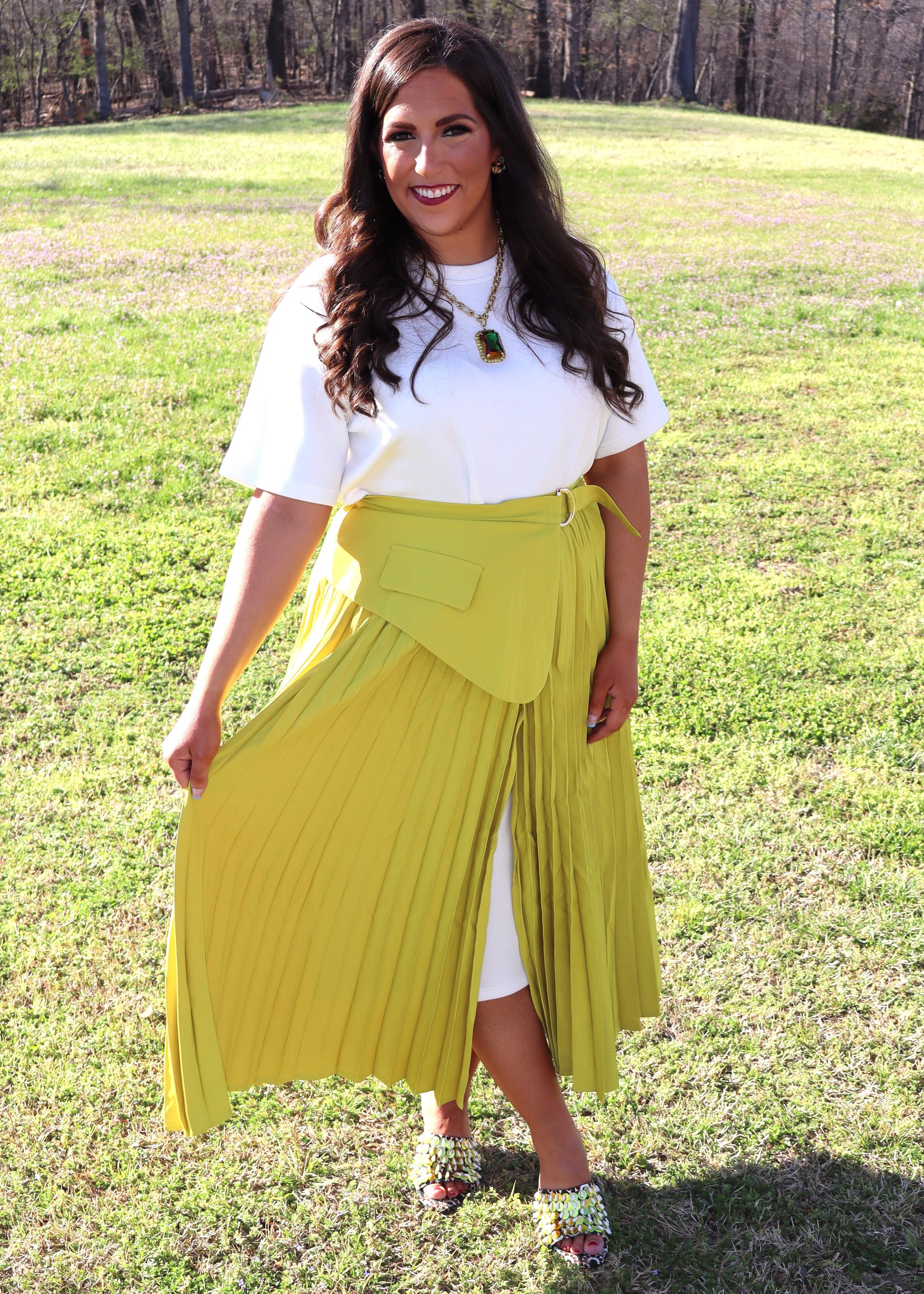 Woman wearing a white top and yellow skirt standing in a grassy field.