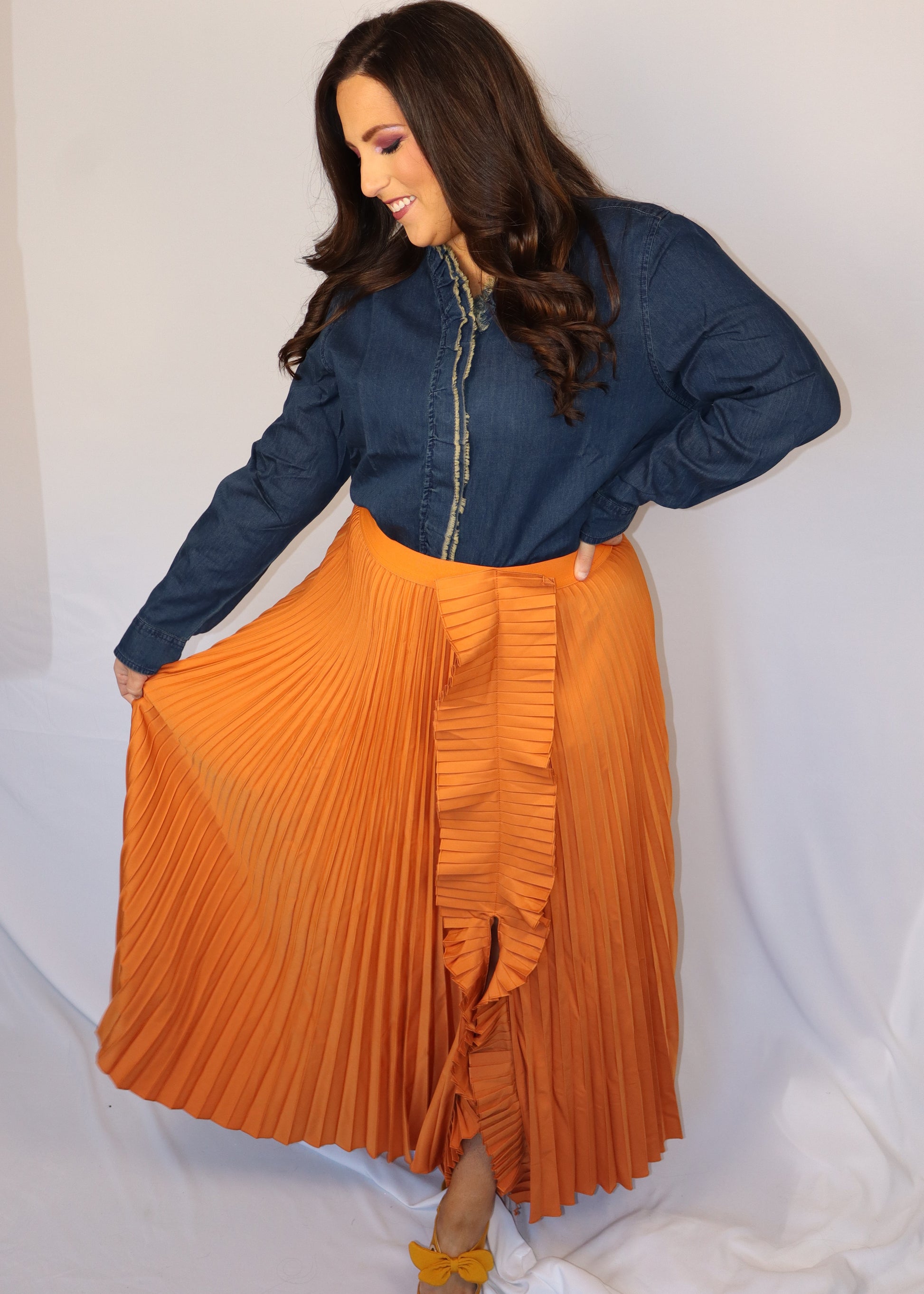 Woman wearing a denim blue top and orange pleated skirt against a white background