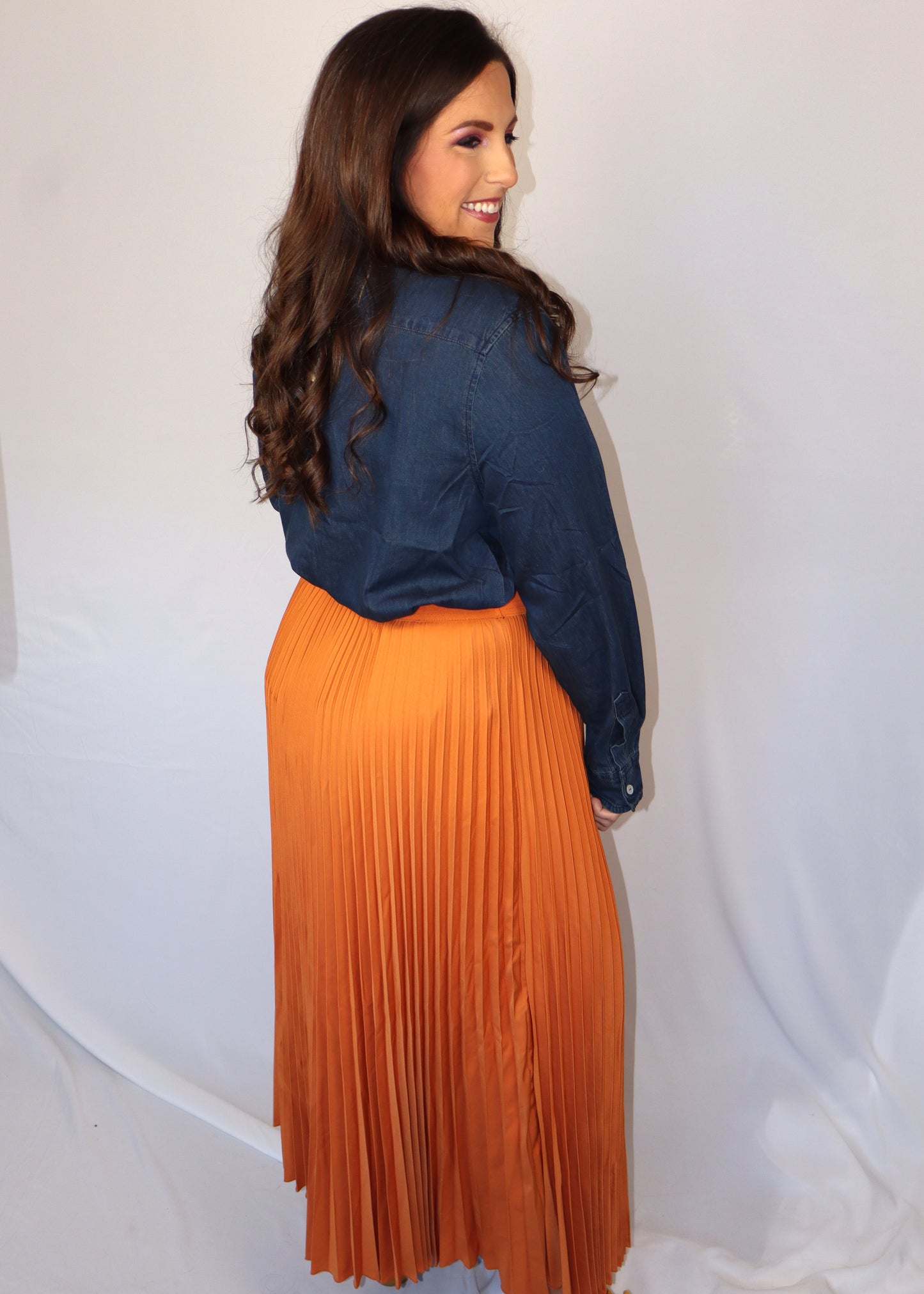Woman wearing a denim blue top and orange pleated skirt against a white background