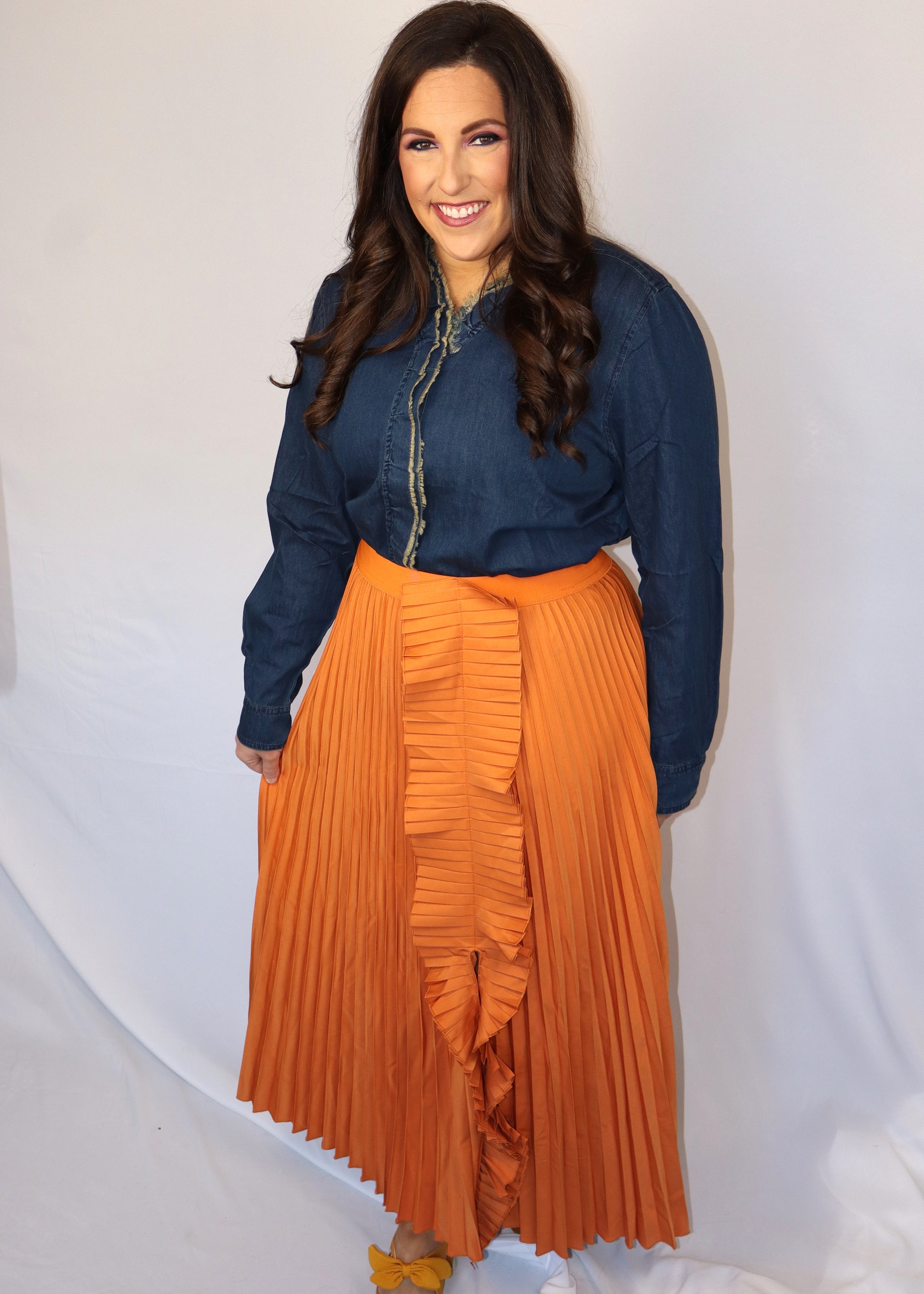 Woman wearing a denim blue top and orange pleated skirt against a white background