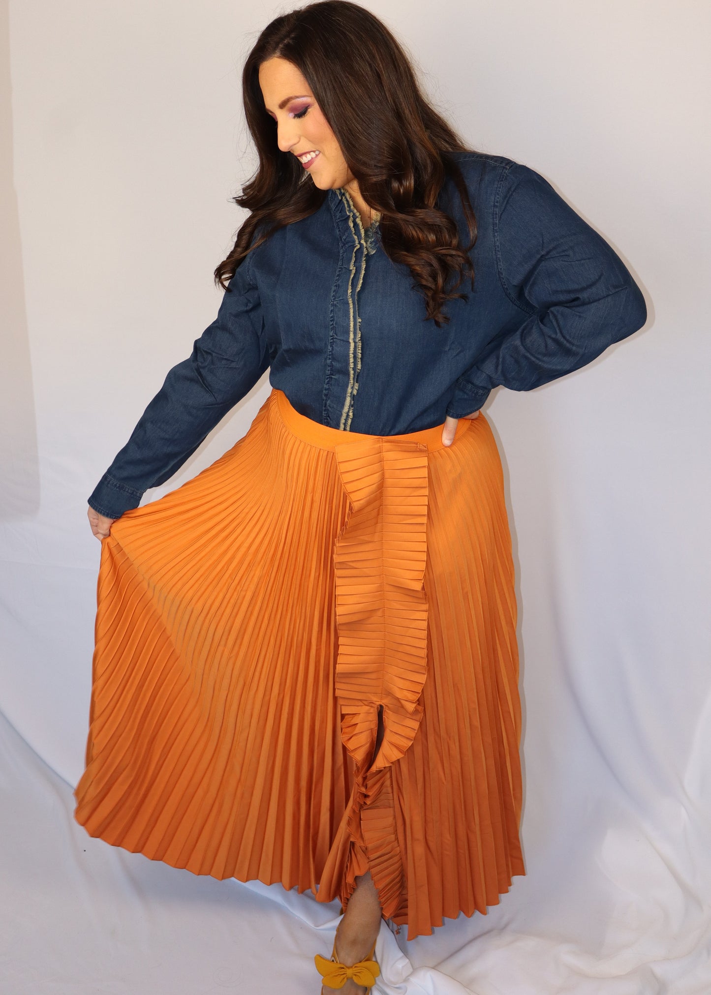Woman wearing a denim blue top and orange pleated skirt against a white background