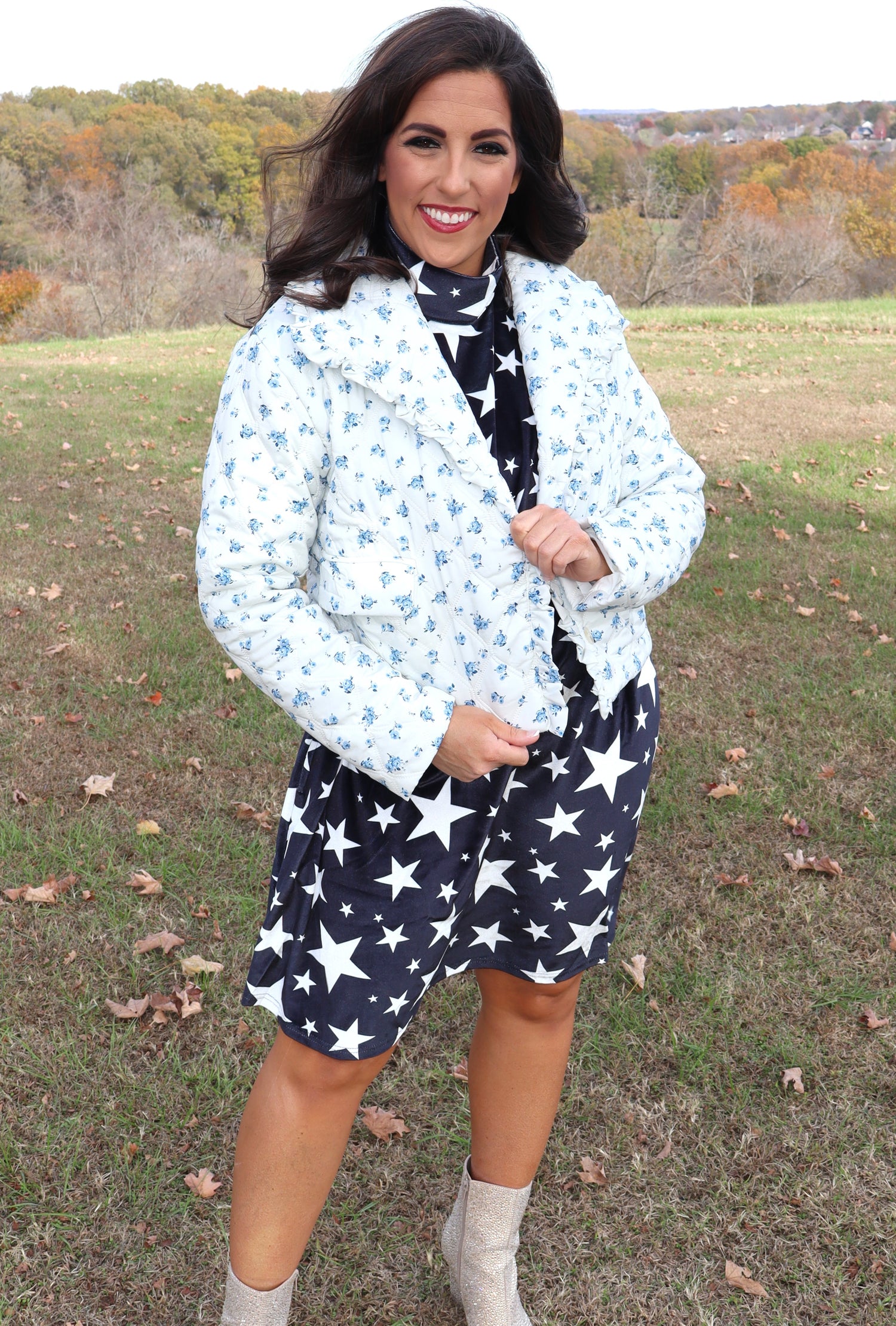 Woman wearing a light blue floral jacket and navy velvet dress with white star pattern outdoors.