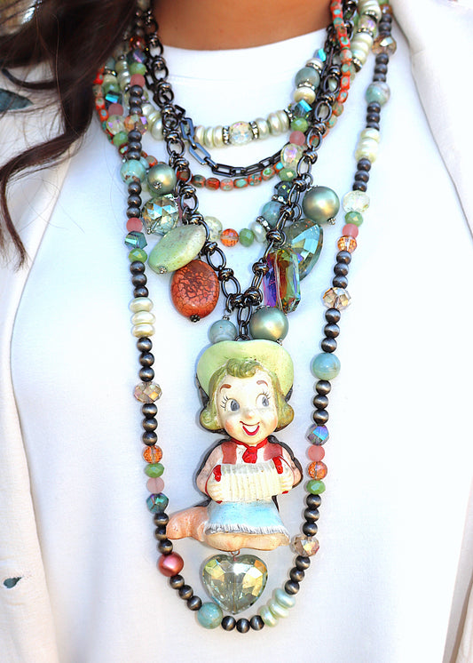 One-of-a-kind, colorful beaded necklace with a vintage-style glass female cowgirl character with her accordion pendant on a white background