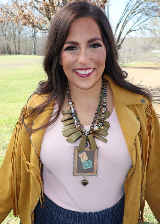 Woman wearing a mustard yellow jacket with a large gold stones and vintage photo pendant Art by Amy necklace outdoors.