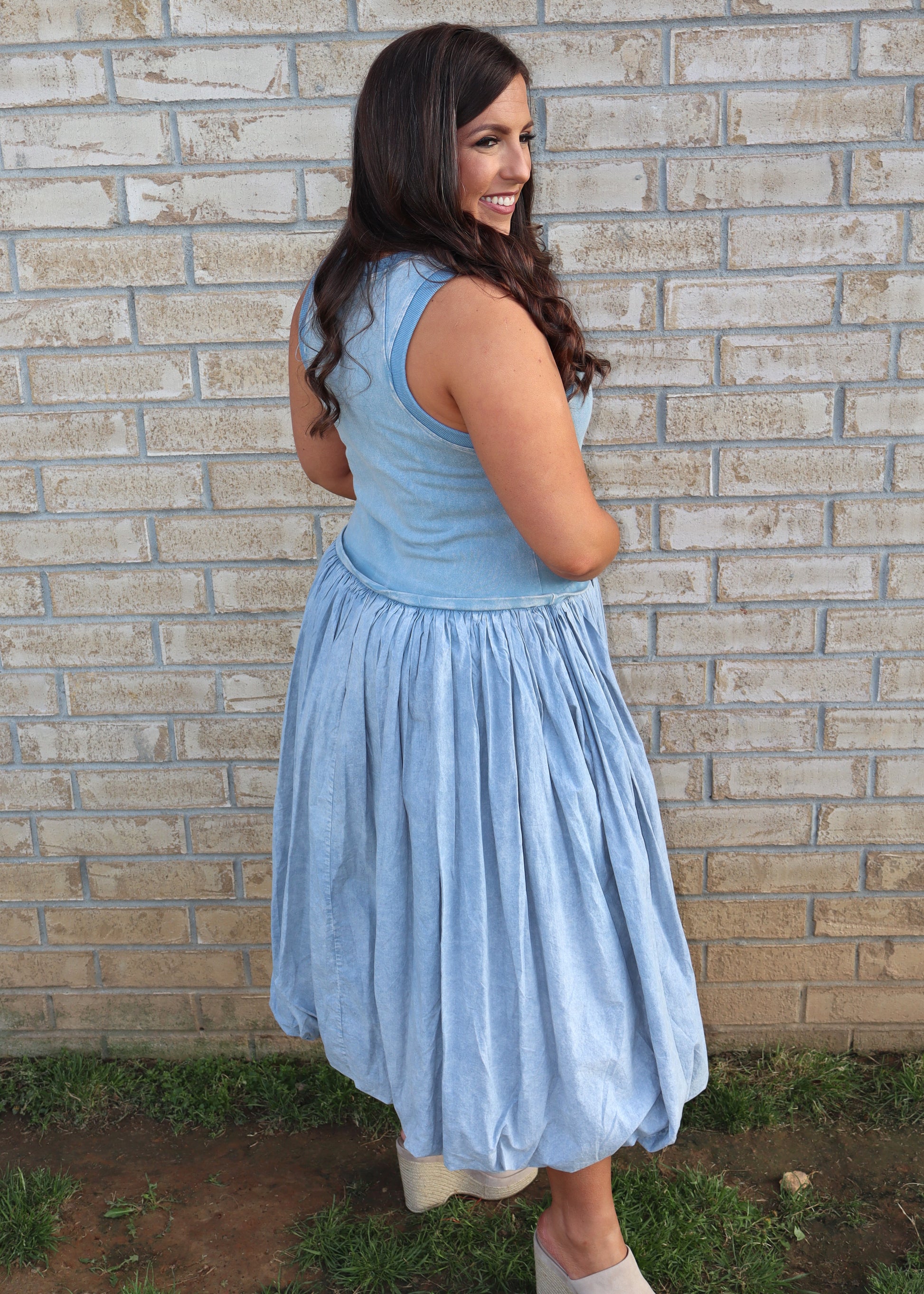 Woman wearing a light blue bubble dress standing against a brick wall.