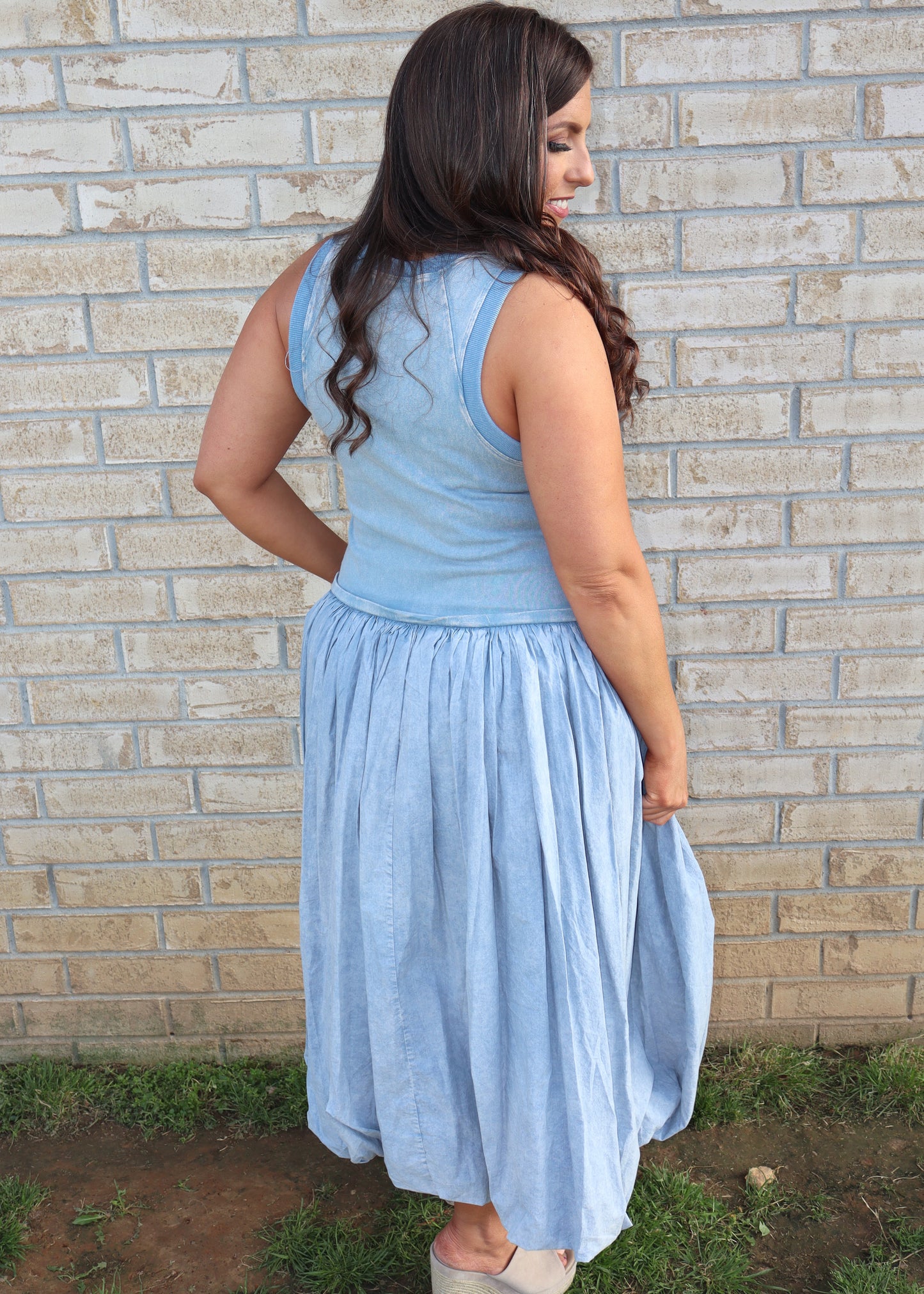 Woman wearing a light blue bubble dress standing against a brick wall.