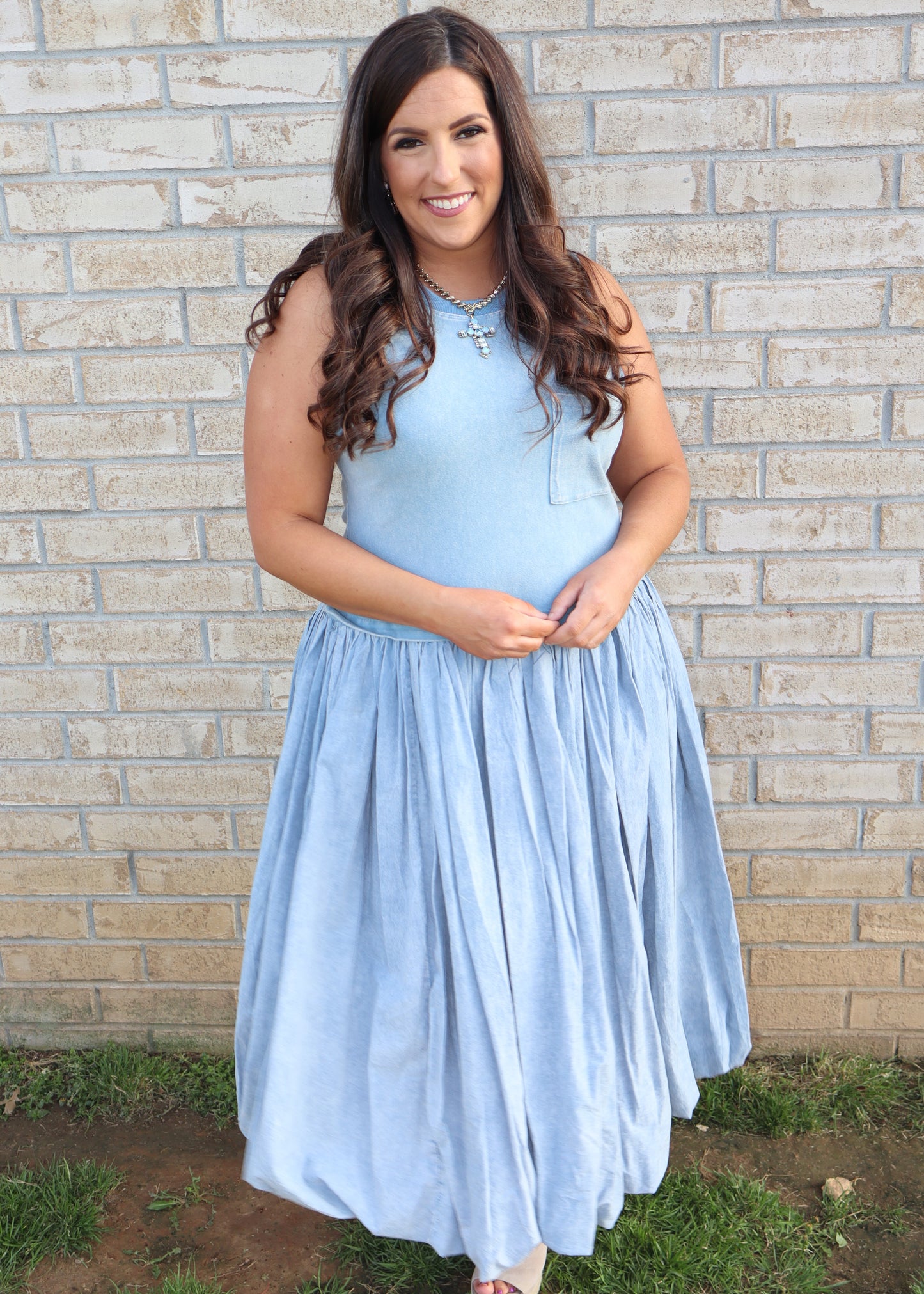 Woman wearing a light blue bubble dress standing against a brick wall.