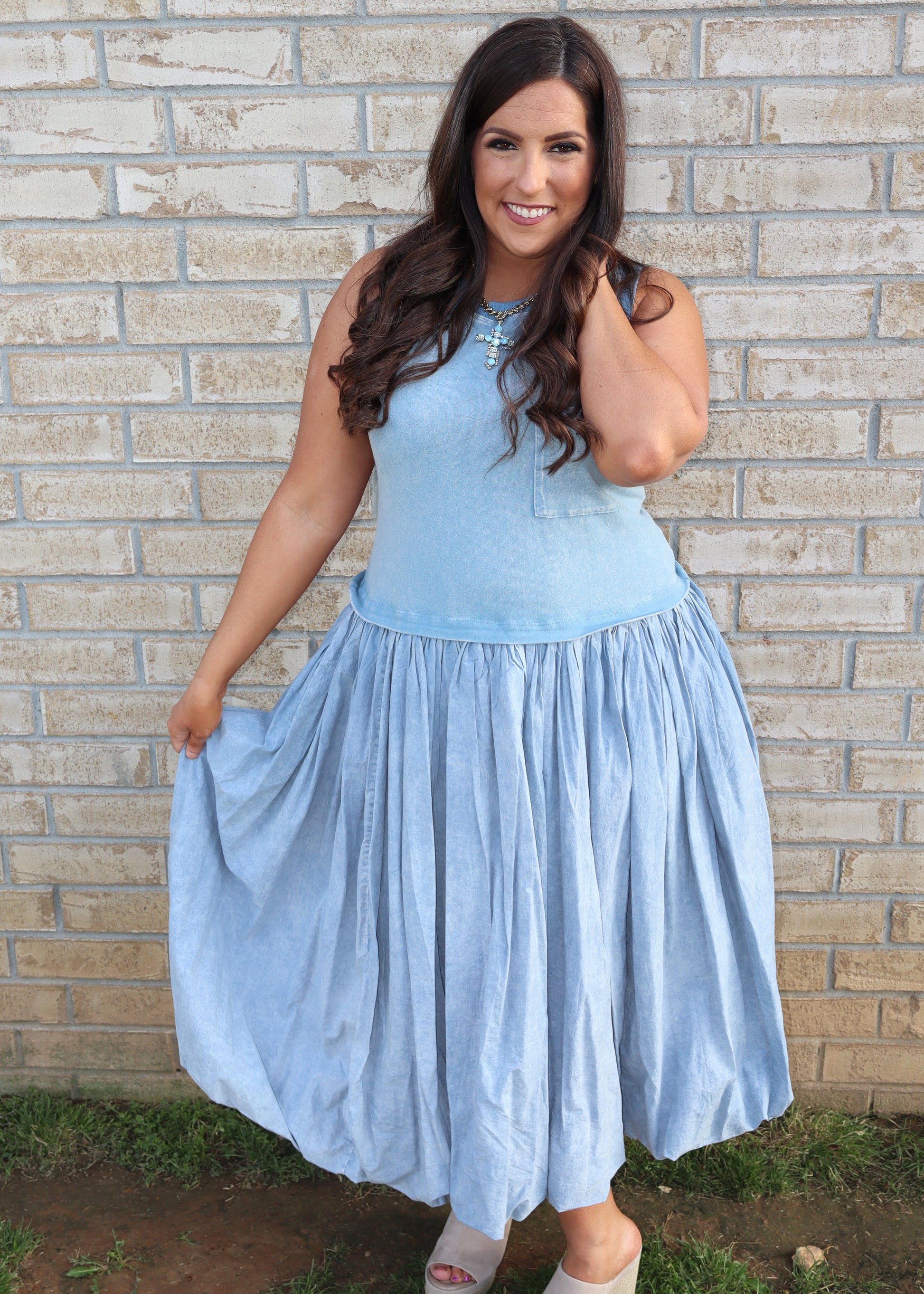 Woman wearing a light blue bubble dress standing against a brick wall.