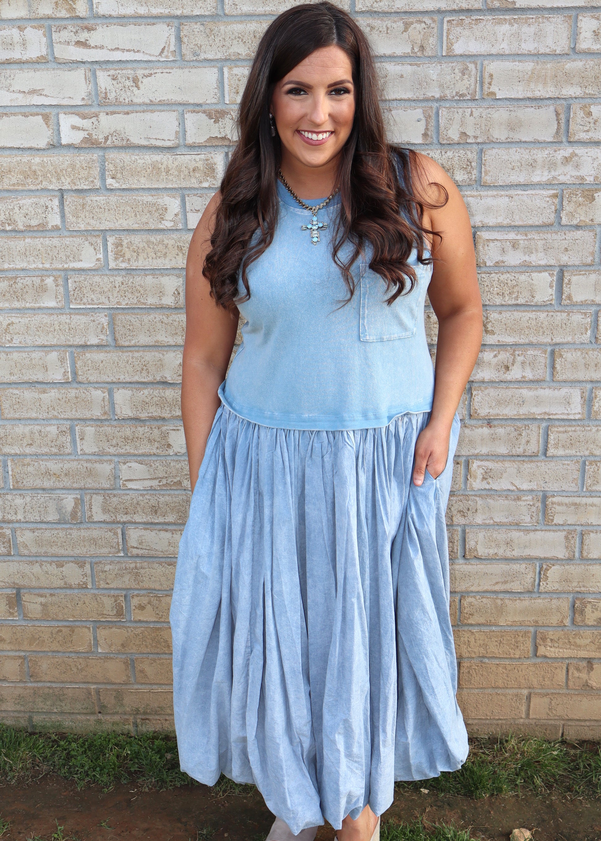 Woman wearing a light blue bubble dress standing against a brick wall.