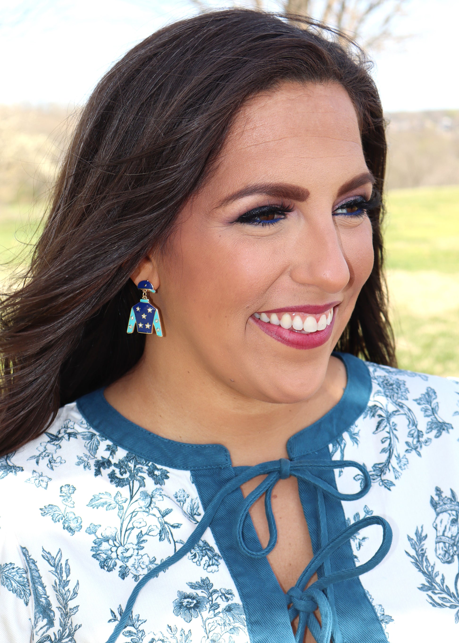 Blue jockey silks earring with stars worn on an ear on a woman wearing a horse-print dress standing outside 