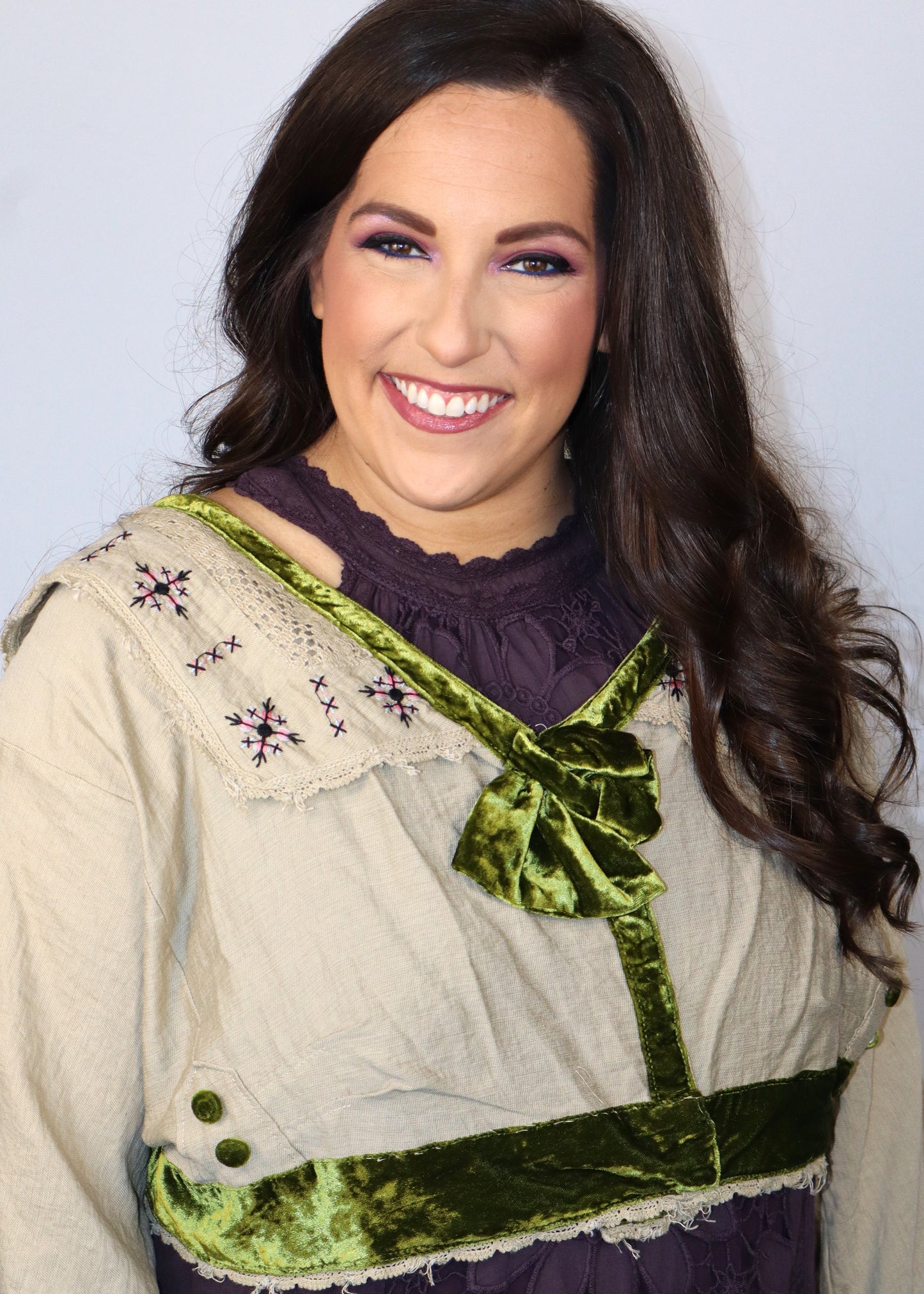Woman wearing a linen neutral cardigan over a plum-colored dress against a plain background. 