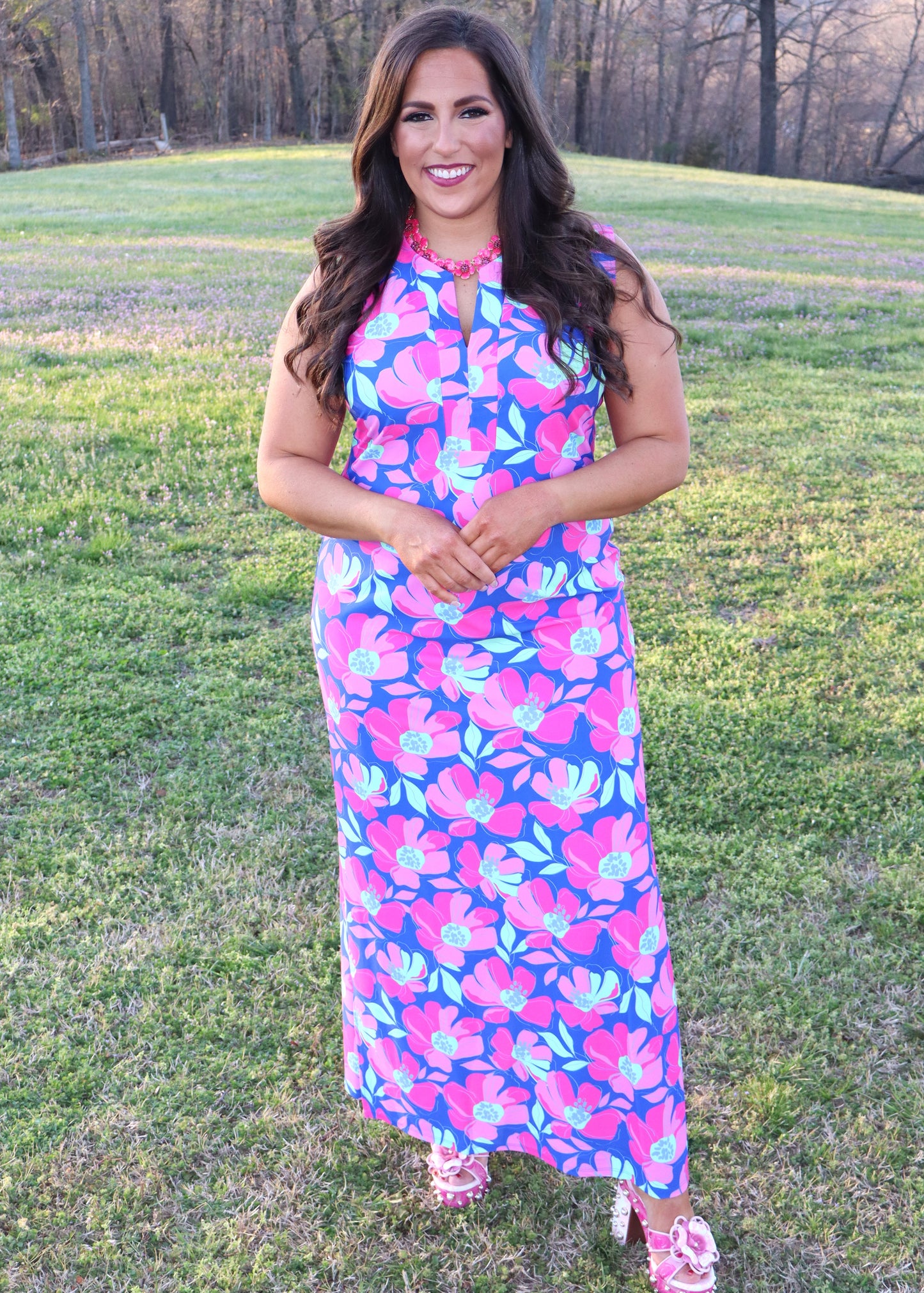 Woman wearing a colorful floral dress standing in a grassy field.