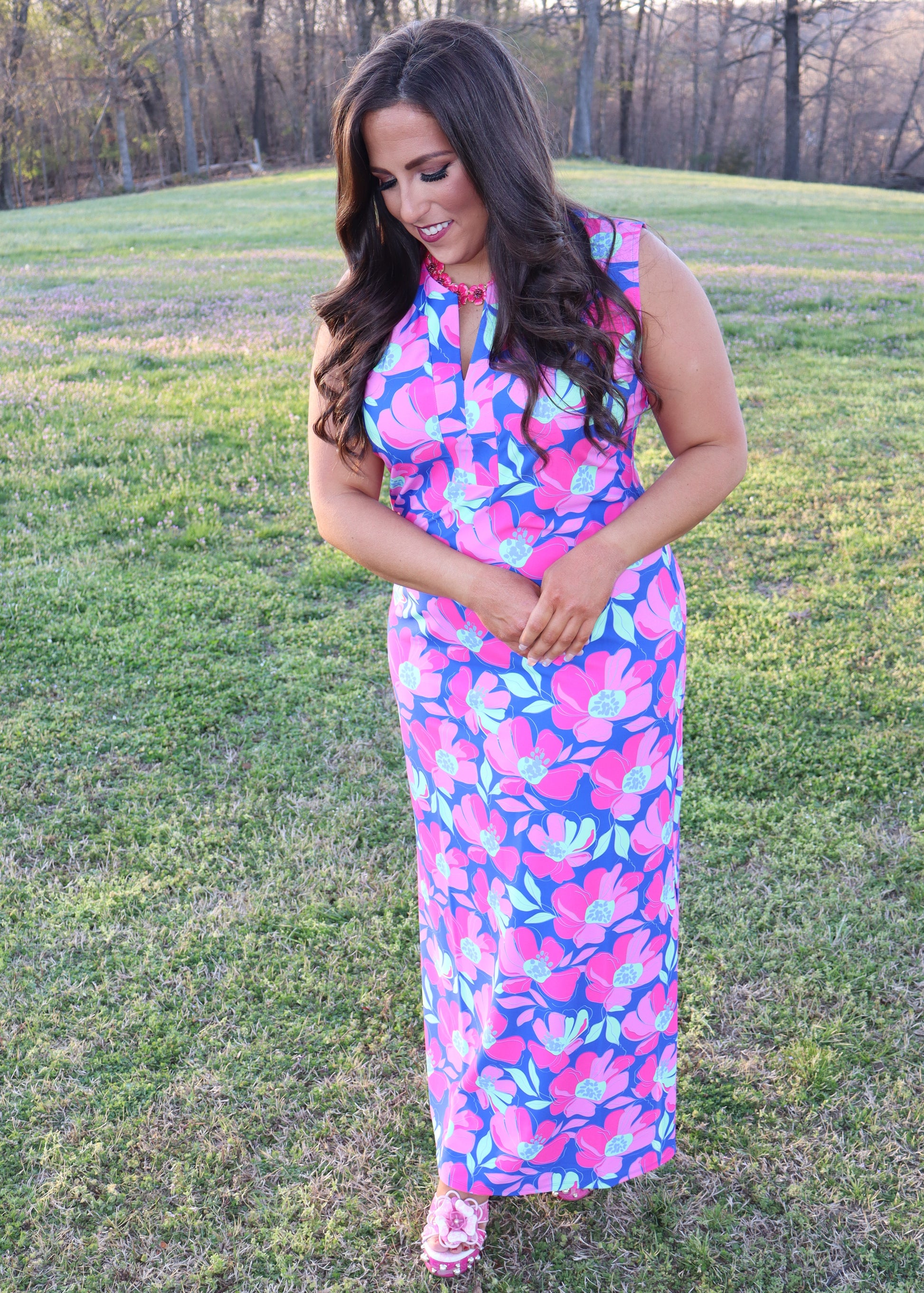 Woman wearing a colorful floral dress standing in a grassy field.