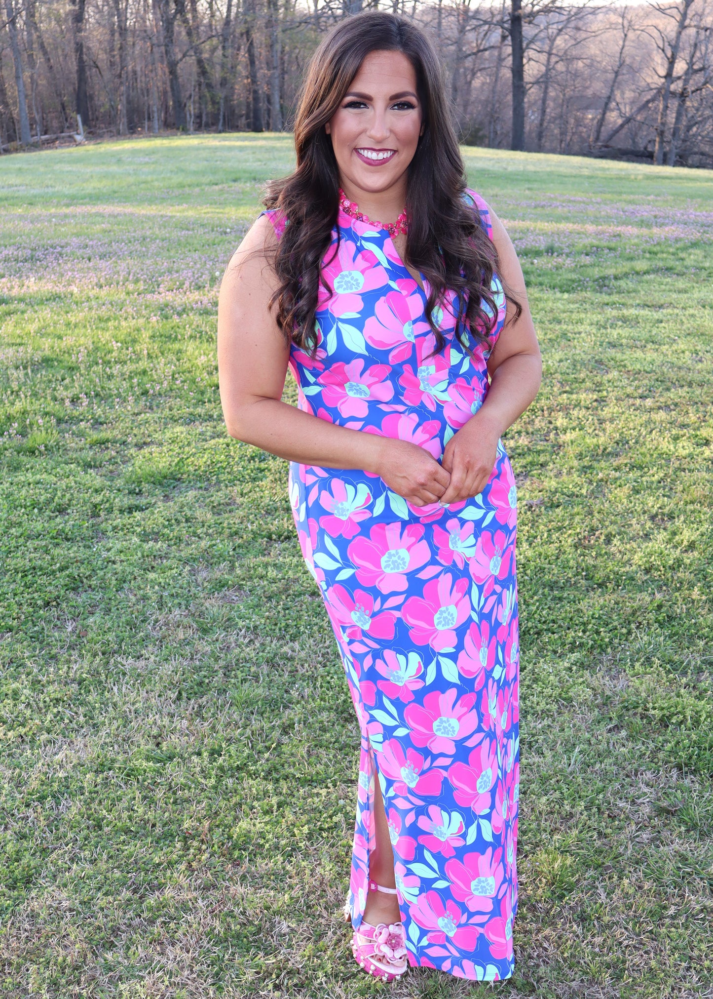 Woman wearing a colorful floral dress standing in a grassy field.