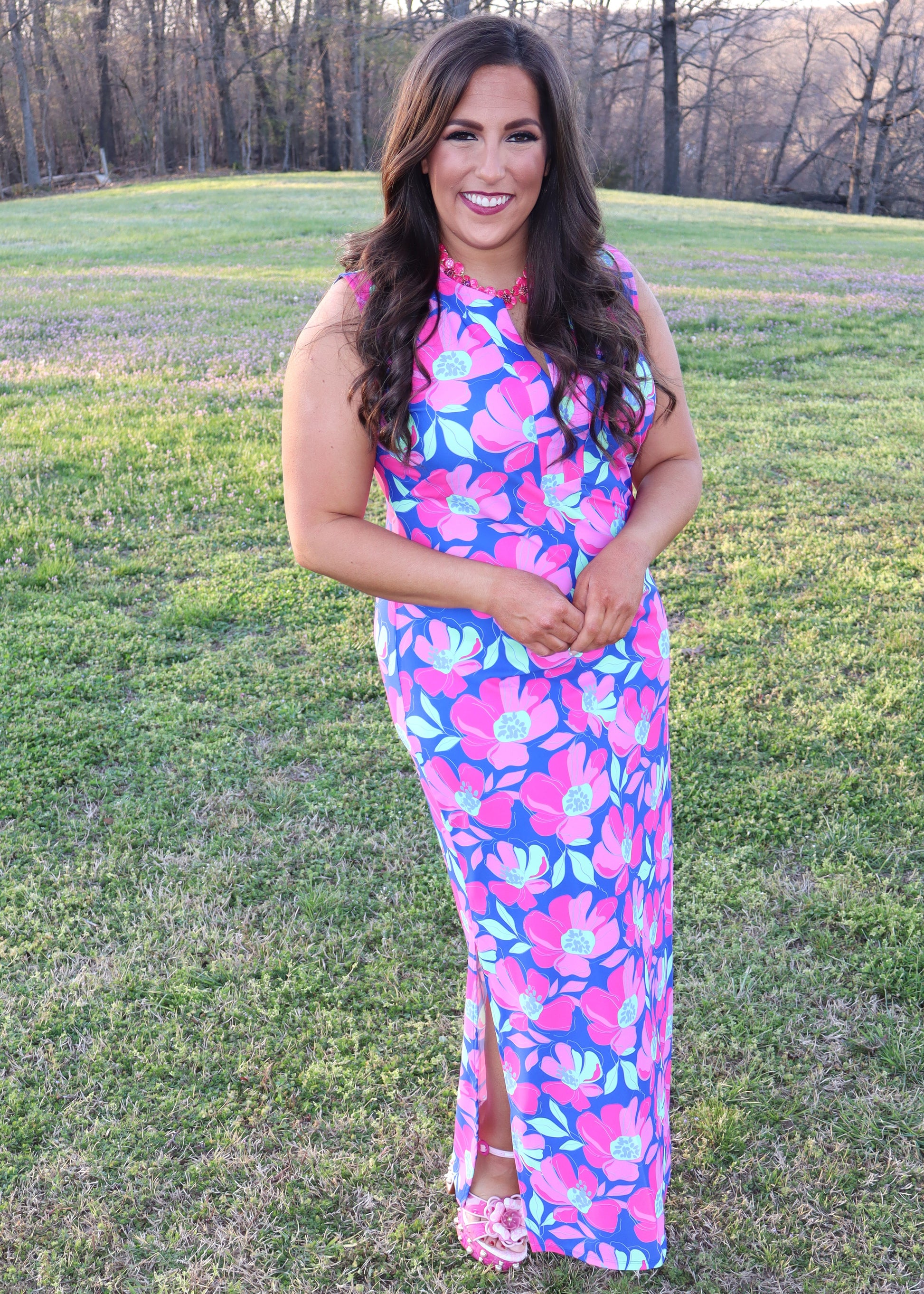 Woman wearing a colorful floral dress standing in a grassy field.