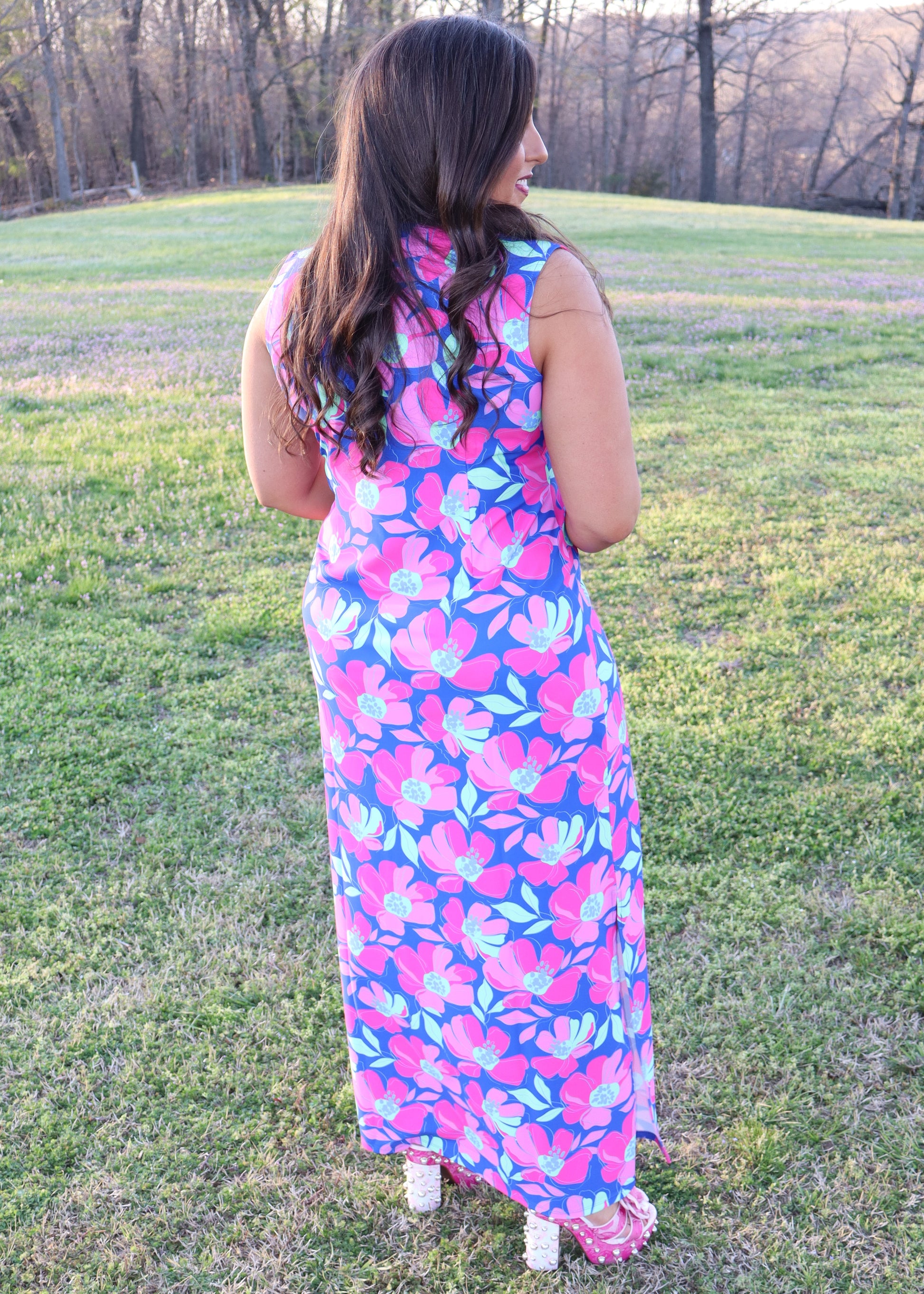 Woman wearing a colorful floral dress standing in a grassy field.