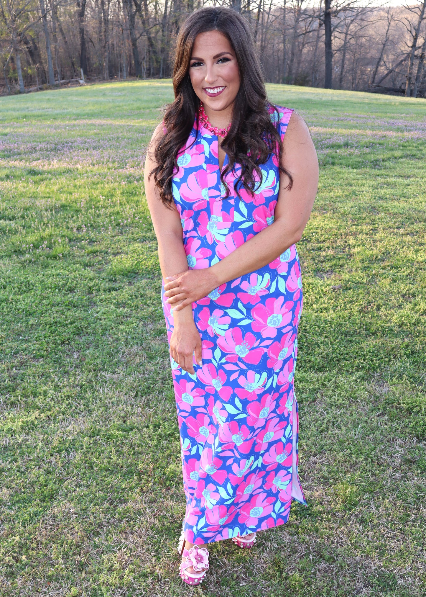 Woman wearing a colorful floral dress standing in a grassy field.
