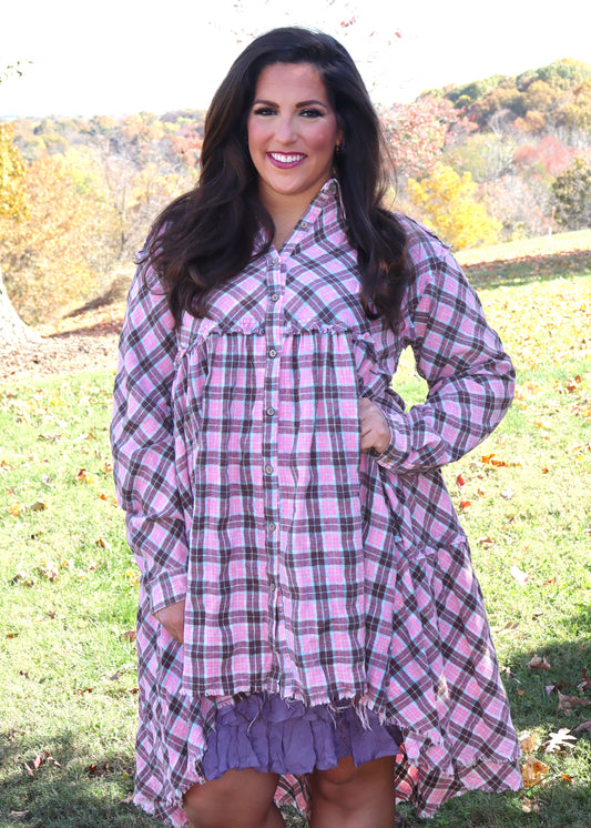 Woman wearing a bubblegum pink and aqua plaid dress with a ruffled slip dress underneath in an outdoor setting with trees in the background.