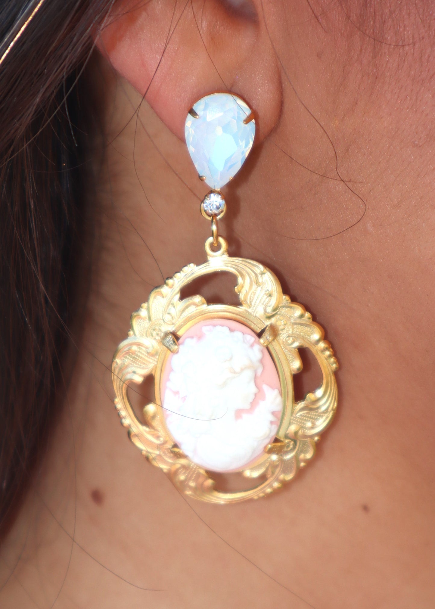 Close-up of an ornate gold earring with a pink cameo worn by a woman