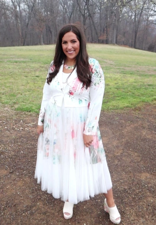 Video of woman wearing a white floral duster standing in a natural setting with grass and dirt.